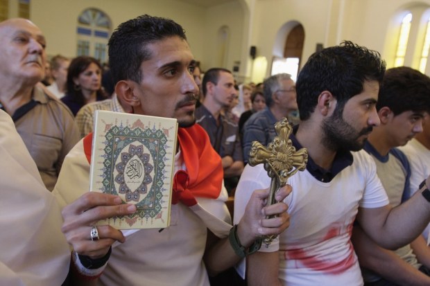 Iraqi man holds up cross and Qur'an at interfaith solidarity event. Source: Buzzfeed